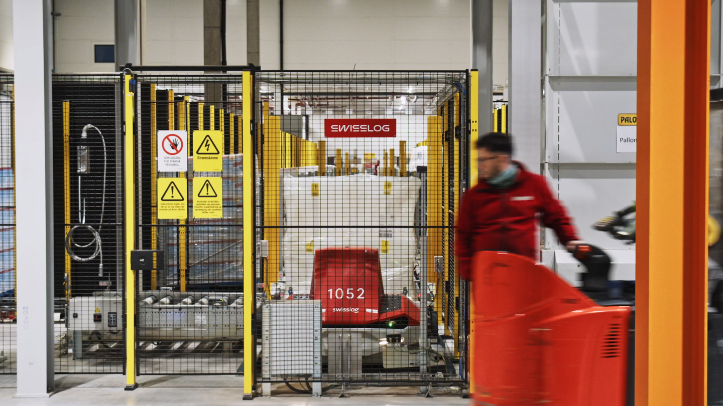 Swisslog AGV behind safety fence in warehouse with worker in front