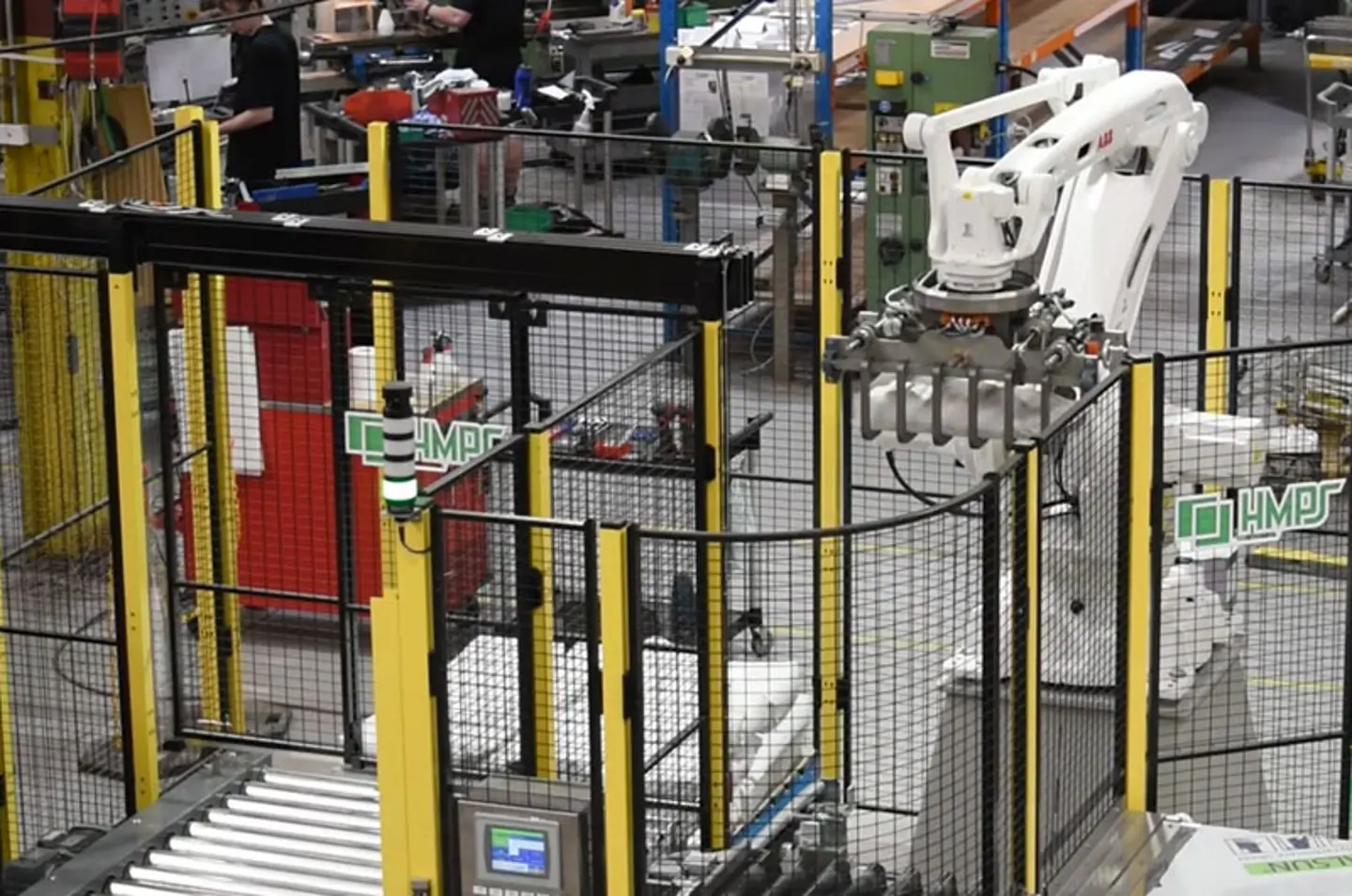 Automatisierter Industrieroboterarm im Betrieb mit Förderanlagen und Schutzeinzäunung in einer Fabrik