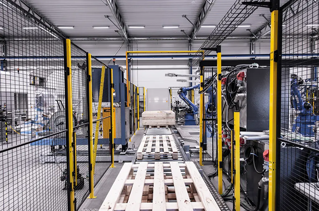Automatisierte Palettieranlage mit Roboterarmen und Paletten in einer gesicherten Zone