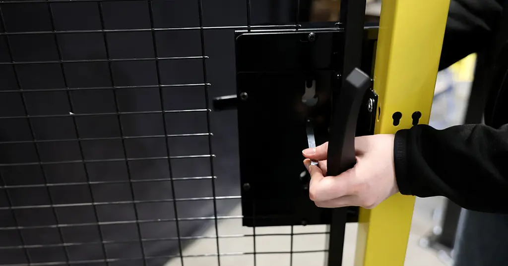 Hand, die ein auf einer schwarzen Gitterplatte montiertes Zylindergriffschloss hält