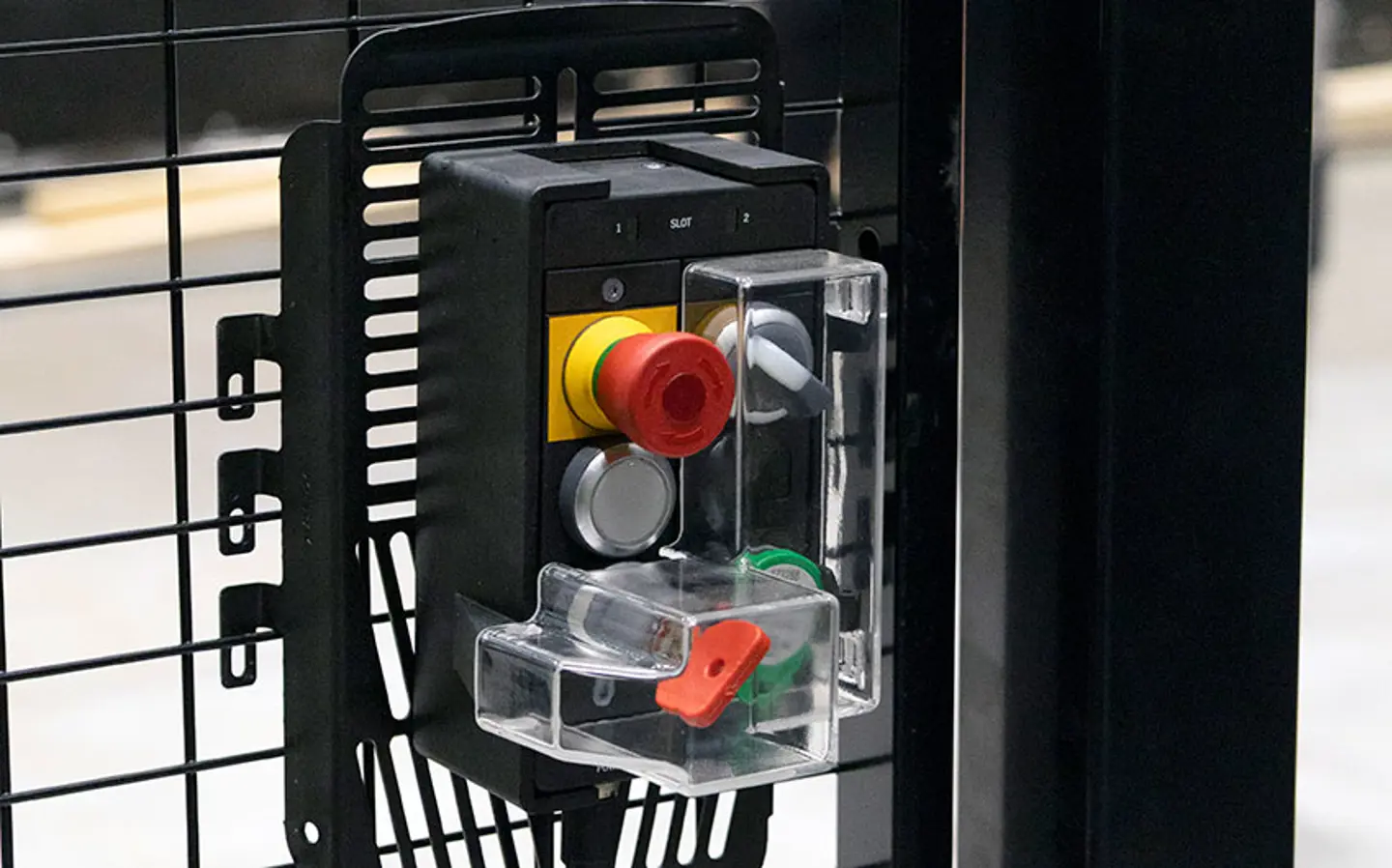 Emergency stop button with protective cover mounted on a metal safety fence